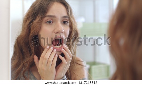 Young woman\
with opened mouth checking teeth in mirror in home bath room.\
Brunette woman looking mouth, teeth and smile front bathroom\
mirror. Teeth care, beauty and health\
concept