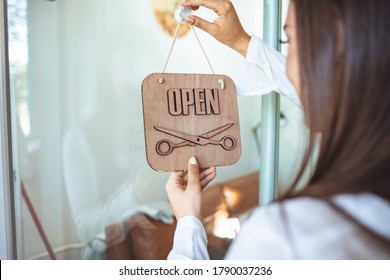 Young Woman Opening A Beauty Store And Looking Very Happy - Small Business Concepts. Smiling Owner Of Hair Salon Standing With Sign Open And Leaning On Glass Door