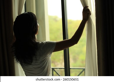 young woman opening curtains bedroom の写真素材 今すぐ編集