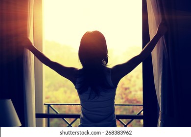 young woman opening curtains in a bedroom - Powered by Shutterstock