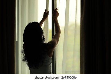 Young Woman Opening Curtains In A Bedroom