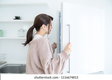 Young woman opening a door of a refrigerator.