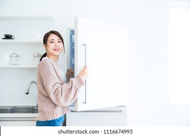 Young Woman Opening A Door Of A Refrigerator.