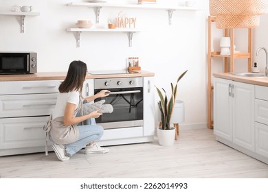 Young woman opening electric oven in kitchen - Shutterstock ID 2262014993
