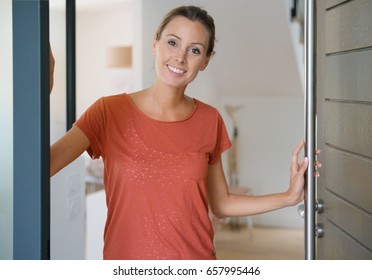 Young Woman Opening House Front Door To Welcome People In