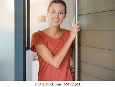Young Woman Opening House Front Door To Welcome People In