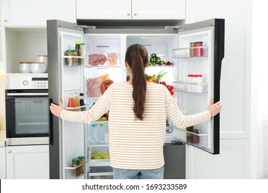 Young Woman Opening Refrigerator In Kitchen, Back View