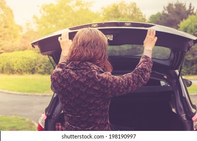 A Young Woman Is Opening The Trunk Of A Car