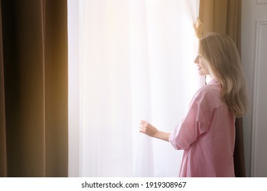 Young Woman Opening Window Curtains At Home