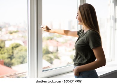 Young Woman Opening Window In Living Room