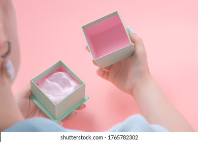 Young Woman Opens A Empty Jewelry Gift, Woman Holding An Open Jewelery Gift Box. Pink Background. Present Concept.