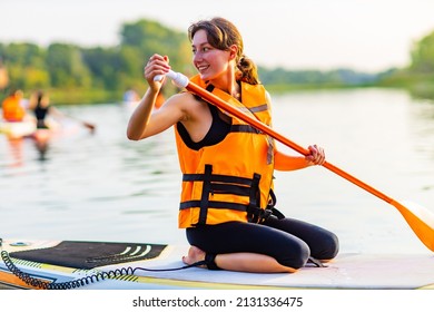 Young Woman In Orange Life Jacket On Supboard At River