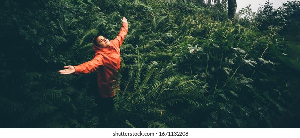 The Young Woman With Orange Raincoat Smiles And Laughs Under The Rain. Girl Enjoying Warm Summer Rain At The Tropical Forest. Сoncept Of Nature And Happy Life With Adventure.