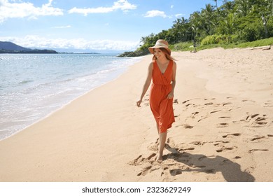 Young woman with orange sundress and straw hat walking on the sand beach - Powered by Shutterstock