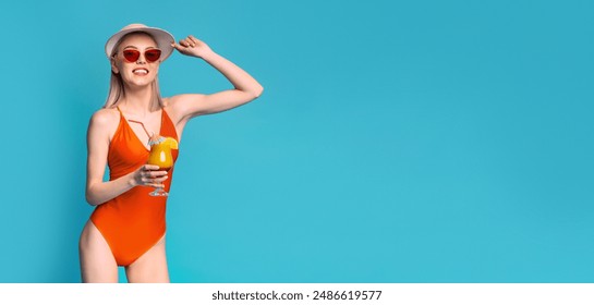 Young woman in an orange swimsuit, wearing sunglasses and a straw hat, holding a cocktail with a straw, standing in front of a solid blue background. She is looking at copy space - Powered by Shutterstock