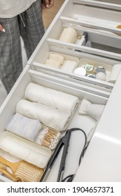 Young woman organizing bathroom storage, displaying beauty cosmetic creams and toiletries into drawer with dividers. Bathroom vanity decluttering concept by using KonMari method.