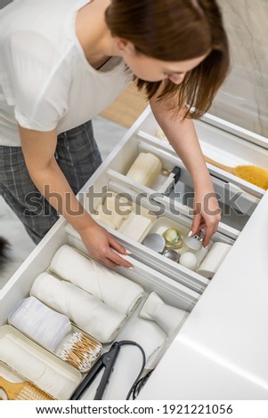 Young woman organizing bathroom storage, displaying beauty cosmetic creams and toiletries into drawer with dividers. Bathroom vanity decluttering concept by using KonMari method.