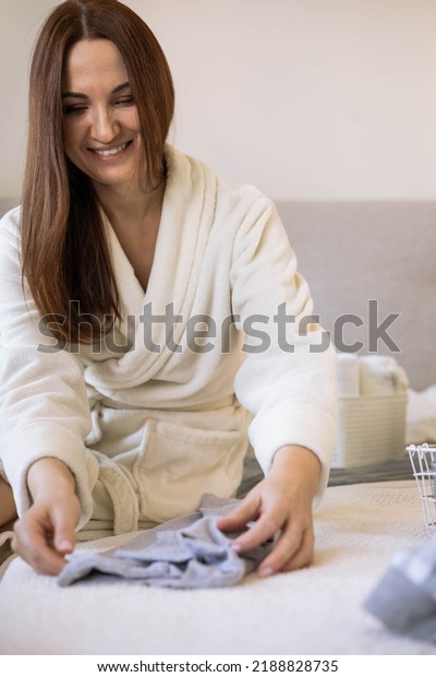 Young woman organizing underwear storage sitting\
on bed at comfortable cozy bedroom. Domestic casual female putting\
clothes into boxes wardrobe. Contemporary folded container cases\
for clothing