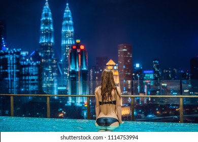 Young woman in outdoor swimming pool with city view at night.
