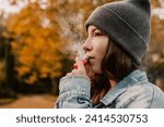 Young woman outside autumn park fall and smoking tobacco device electronic cigarette heater. Smoke and steam system with sticks inside, image with copy space. Harmful habit harm to health lungs

