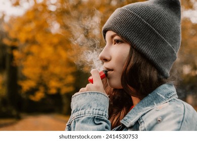 Young woman outside autumn park fall and smoking tobacco device electronic cigarette heater. Smoke and steam system with sticks inside, image with copy space. Harmful habit harm to health lungs

