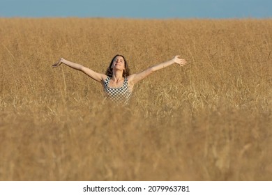Young woman with outstretched arms standing half-covered in wheat field on a sunny day