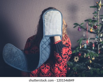 A Young Woman With Oven Gloves Is Standing By The Christmas Tree