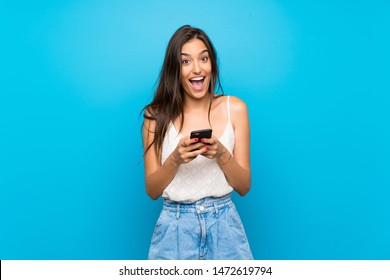 Junge Frau einzeln auf blauem Hintergrund überrascht und sendet eine Nachricht