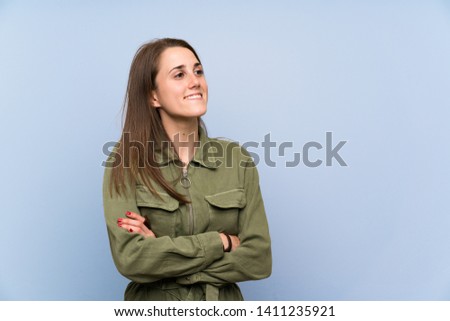 Young woman over isolated blue wall standing and looking to the side