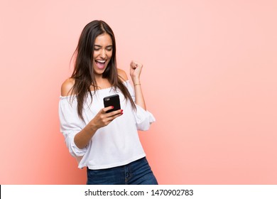 Junge Frau auf einzeln rosafarbenem Hintergrund mit Telefon in Siegesposition