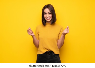 Young Woman Over Yellow Wall Making Money Gesture