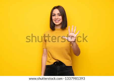 Young woman over yellow wall counting five with fingers