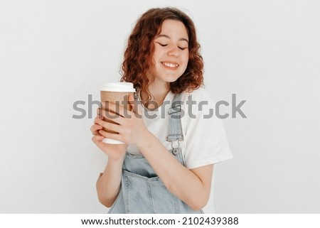Young woman with overalls holding a hot cup of coffee, over white wall. Free time concept
