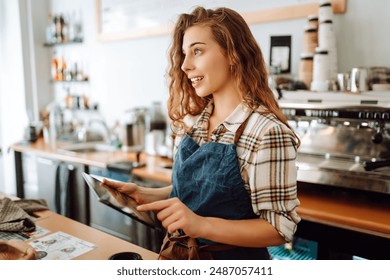 Young woman owner with tablet stands behind the counter of a coffee shop. Business concept. Takeaway food. - Powered by Shutterstock