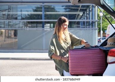 Young Woman Packing Her Suitcase Into Luggage Boot Of The Car. Holidays Concept.