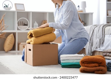 Young woman packing stack of clothes into cardboard box in bedroom - Powered by Shutterstock