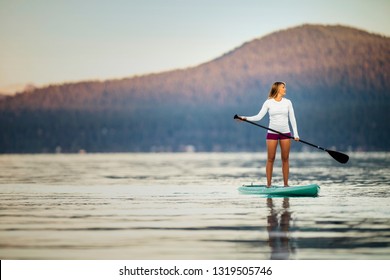 Young Woman Paddle Boarding On A Lake.