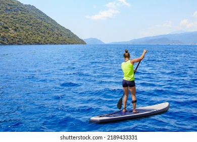 Young woman paddleboarding on a SUP board in the Mediterranean Sea. Supsurfing is a popular outdoor activity. Stand up paddle boarding