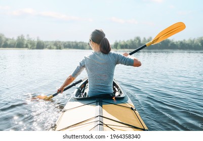 Young woman paddling in yellow color kayak on calm lake on sunny summer day, rear view. - Powered by Shutterstock