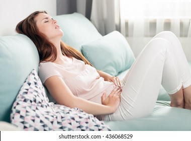 Young Woman In Pain Lying On Couch At Home, Casual Style Indoor Shoot