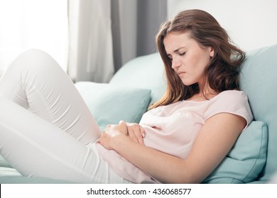 Young woman in pain lying on couch at home, casual style indoor shoot