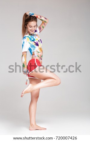 young woman with paint brush is dirty in multicolored paint. girl is fooling around