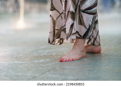 Young Woman With Painted Pink Nails Stands In The Middle Of Jet Fountain. She's Barefoot. A Hot Summer Day. The Concept Of Freshness And Relaxation On A Day Off In The Big City Moscow. Close Up Image