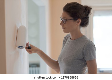 Young woman painting walls at home with a paint roller: home makeover concept - Shutterstock ID 1179938956