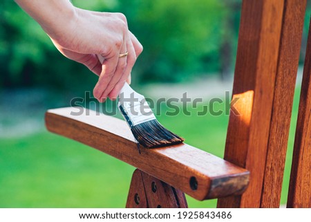 young woman painting wooden exotic chair in the garden with a brush - shallow depth of field