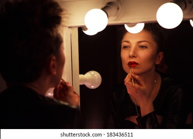 Young Woman Paints Lips In Red In The Dressing Room In The Dark Before A Mirror