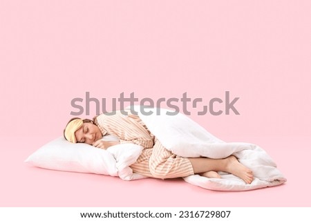 Young woman in pajamas with blanket and pillow sleeping on pink background