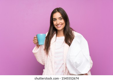 Young Woman In Pajamas And Dressing Gown Over Isolated Purple Background Holding A Cup Of Coffee