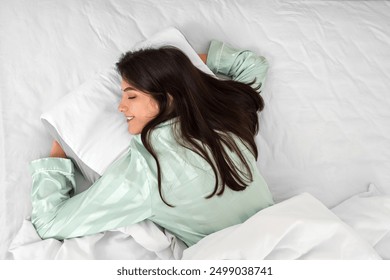 Young woman in pajamas lying on soft orthopedic pillow on comfortable bed at home