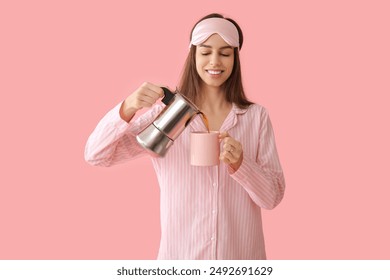 Young woman in pajamas and mask holding cup and coffee pot on pink background